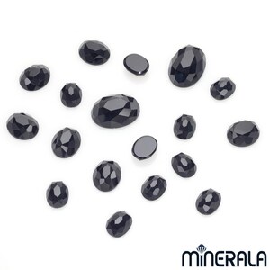 Peut inclure: Une collection de pierres pr&eacute;cieuses ovales noires, certaines l&eacute;g&egrave;rement facett&eacute;es, dispos&eacute;es sur une surface blanche.