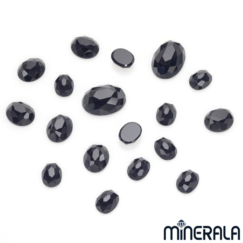 Peut inclure: Une collection de pierres pr&eacute;cieuses ovales noires, certaines l&eacute;g&egrave;rement facett&eacute;es, dispos&eacute;es sur une surface blanche.