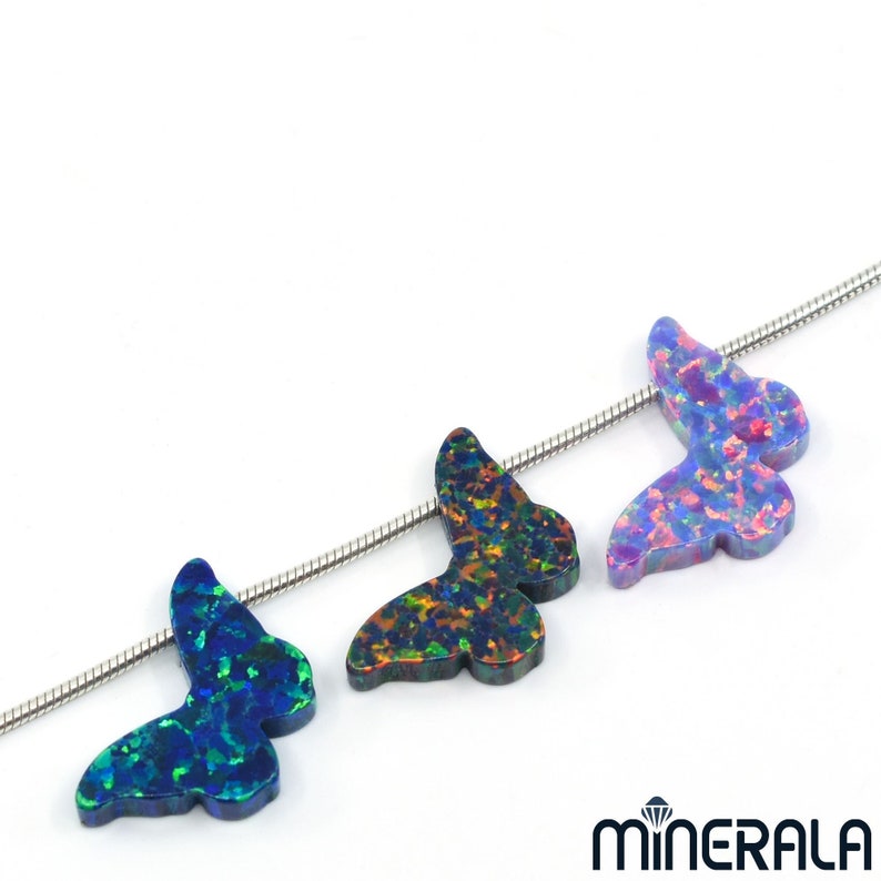 Puede incluir: Tres abalorios de mariposa de &oacute;palo en una cadena de plata. Las mariposas son iridiscentes con tonos de azul, verde y morado.