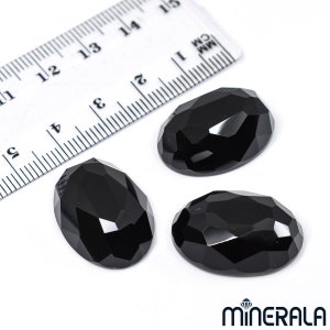 Peut inclure: Trois pierres pr&eacute;cieuses noires de forme ovale avec des bords facet&eacute;s. Les pierres pr&eacute;cieuses mesurent environ 2,5 cm de long et sont pr&eacute;sent&eacute;es sur une surface blanche &agrave; c&ocirc;t&eacute; d'une r&egrave;gle.