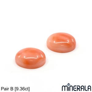 May include: Pair of oval-shaped coral cabochons, each measuring approximately 9.36 carats. The coral is a light pink color with a smooth, polished surface.