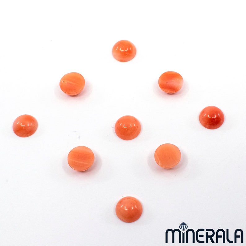 Pu&ograve; includere: Nove cabochon rotondi in corallo liscio, in varie tonalit&agrave; di arancio e rosa. I cabochon sono disposti in modo sparso su uno sfondo bianco.