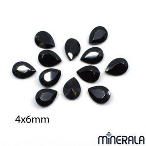 Puede incluir: Un conjunto de gemas negras en forma de l&aacute;grima, cada una de 4x6mm, dispuestas sobre un fondo blanco. Las gemas tienen un dise&ntilde;o facetado, que refleja la luz. La imagen incluye el texto "4x6mm" y el logotipo de la marca "MINERALA".