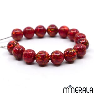May include: A bracelet made of round, red-colored beads with a swirling pattern of orange and green. The beads are strung together on a thin, silver-colored string. The beads are approximately 0.5 inches in diameter.