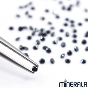 May include: A close-up of a black diamond held by tweezers, surrounded by a scattering of loose black diamonds on a white surface. The image is labelled "MINERALA".