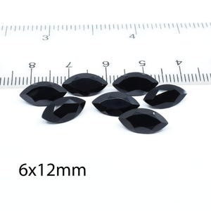 以下が含まれることがあります： 約6x12mmの黒いマーキス型の宝石が7つ、白い面に定規と一緒に並んでいます。宝石はファセット加工されており、光を反射しています。「6x12mm」の文字が見えます。