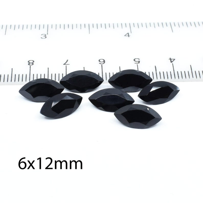 以下が含まれることがあります： 約6x12mmの黒いマーキス型の宝石が7つ、白い面に定規と一緒に並んでいます。宝石はファセット加工されており、光を反射しています。「6x12mm」の文字が見えます。