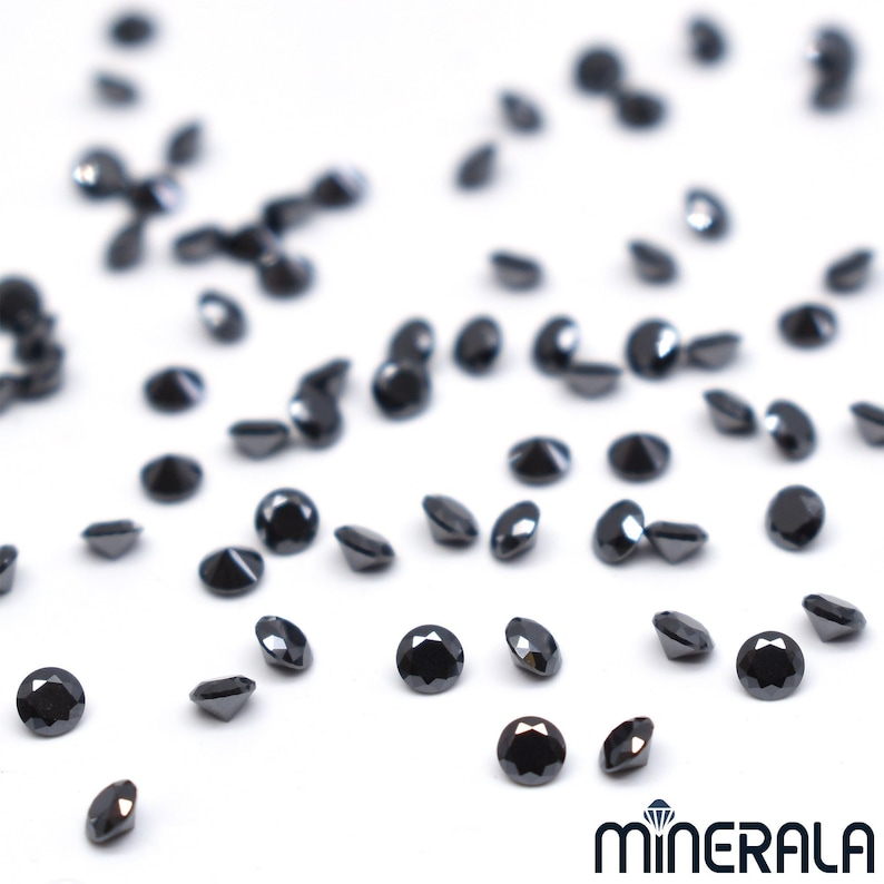 May include: A scattering of black diamonds on a white surface. The diamonds are round and have a high polish.