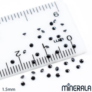 May include: A ruler with black diamond-shaped gemstones scattered on a white surface. The ruler is marked in millimetres and shows a measurement of 1.5mm.