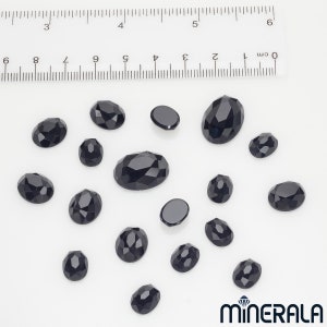 Peut inclure: Une collection de 17 pierres pr&eacute;cieuses ovales noires de tailles diff&eacute;rentes. Les pierres pr&eacute;cieuses sont facett&eacute;es et ont une finition brillante. Les pierres pr&eacute;cieuses sont dispos&eacute;es sur une surface blanche.