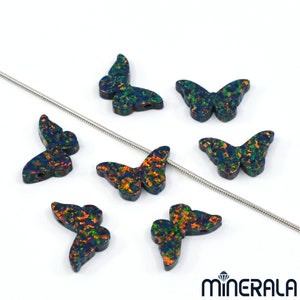 Puede incluir: Siete abalorios de mariposa de &oacute;palo iridiscente con una cadena plateada en el fondo. Las mariposas son de color azul oscuro con acentos iridiscentes verdes, naranjas y rojos.