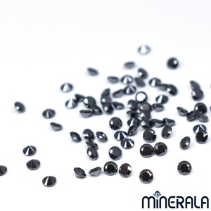 May include: A scattering of black diamonds on a white surface. The diamonds are round and have a brilliant cut.