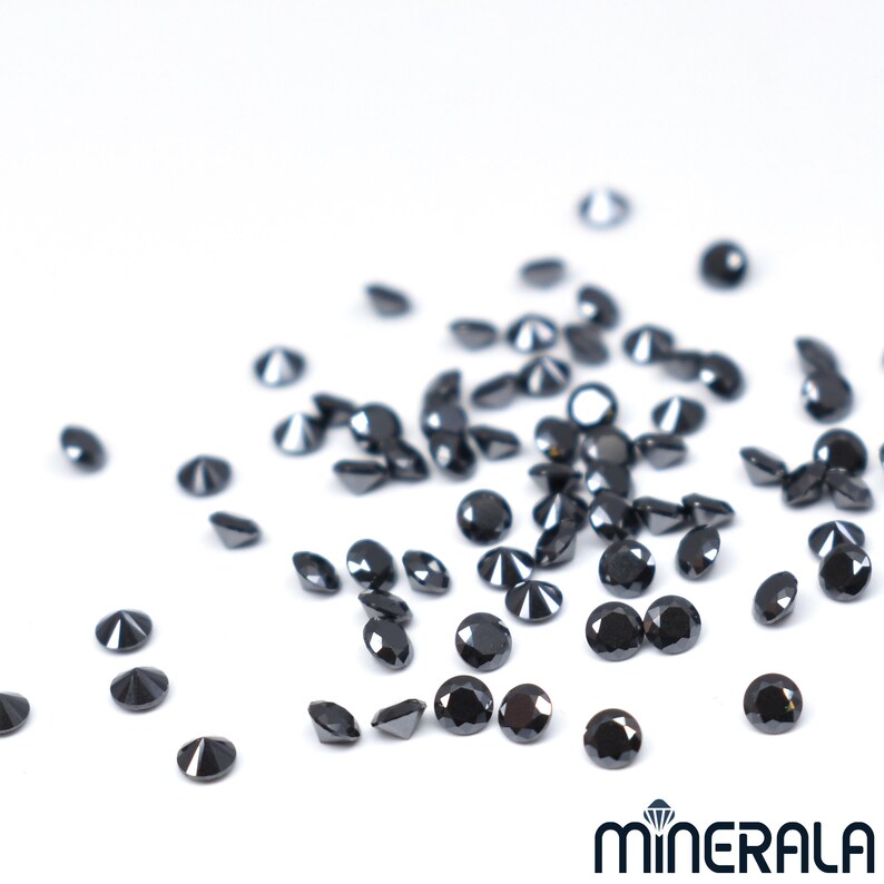 May include: A scattering of black diamonds on a white surface. The diamonds are round and have a brilliant cut.