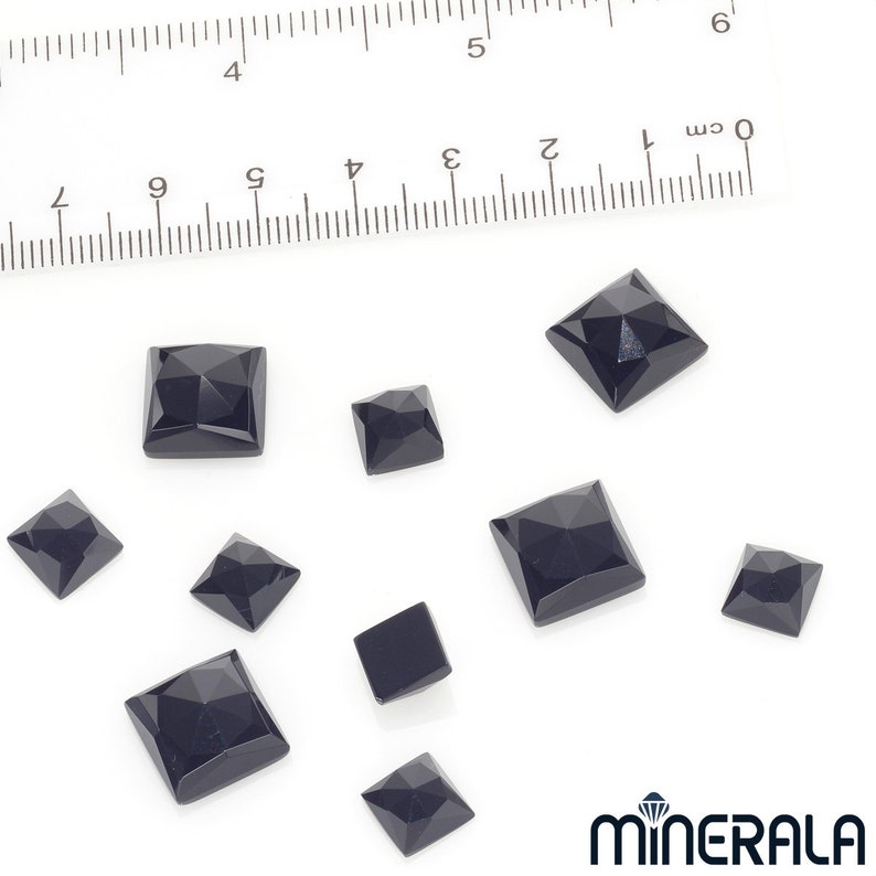 Puede incluir: Colecci&oacute;n de gemas negras facetadas, de corte cuadrado y de varios tama&ntilde;os. Una regla con marcas de cent&iacute;metros se encuentra en el fondo. Las gemas est&aacute;n dispuestas sobre una superficie blanca. El logotipo de Minerala est&aacute; en la esquina inferior derecha.
