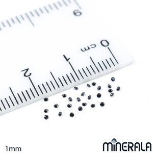 May include: A close-up of a ruler measuring 1 mm with a scattering of small, black, round gemstones.