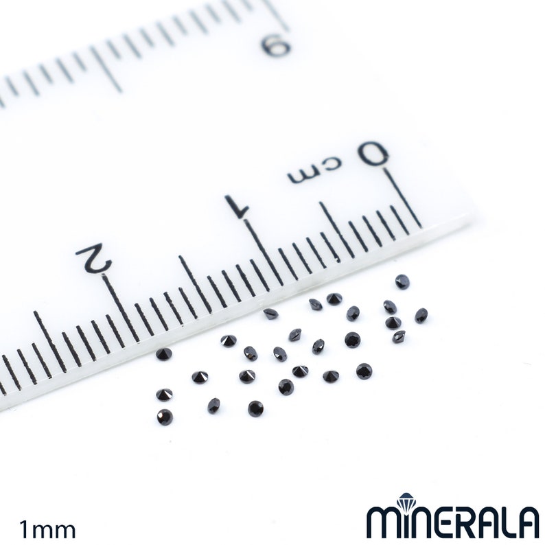 May include: A close-up of a ruler measuring 1 mm with a scattering of small, black, round gemstones.