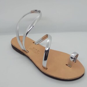 Puede incluir: Sandalias de cuero plateadas con un anillo para el dedo del pie y m&uacute;ltiples correas. Las sandalias est&aacute;n hechas en Grecia y tienen una suela de cuero marr&oacute;n.