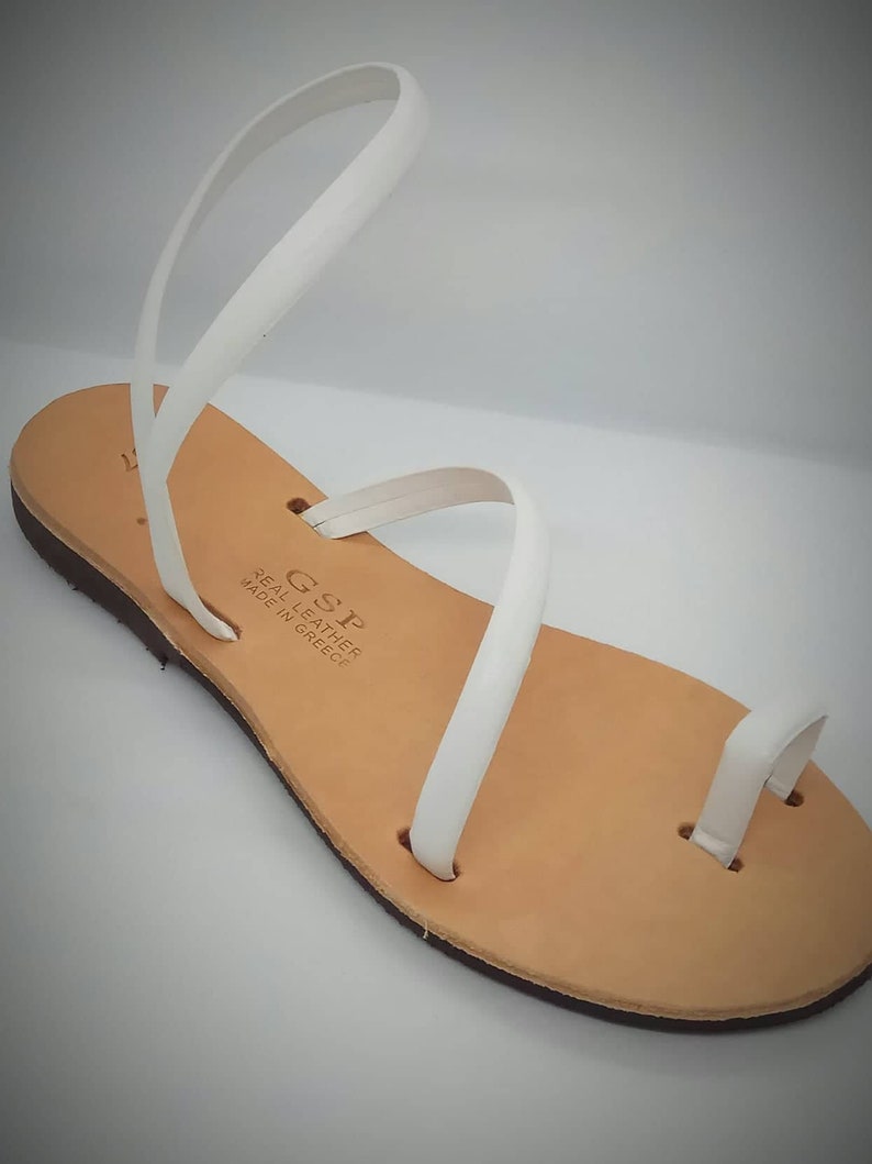 Puede incluir: Sandalias de cuero blanco con una sola correa sobre el pie y un bucle para el dedo del pie. Las sandalias est&aacute;n hechas en Grecia y tienen una suela de cuero marr&oacute;n.