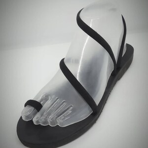 Puede incluir: Sandalias de cuero negro con un dise&ntilde;o sencillo y tiras finas. Las tiras se envuelven alrededor del tobillo y el dedo del pie.