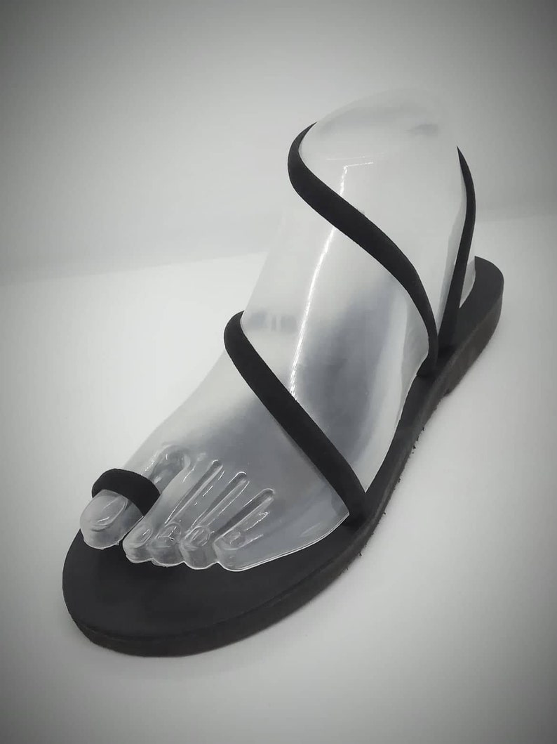 Puede incluir: Sandalias de cuero negro con un dise&ntilde;o sencillo y tiras finas. Las tiras se envuelven alrededor del tobillo y el dedo del pie.