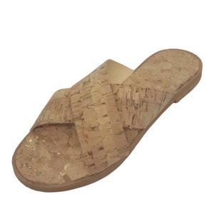 May include: Cork sandals with a criss-cross strap design. The sandals are a light brown color and have a flat sole.