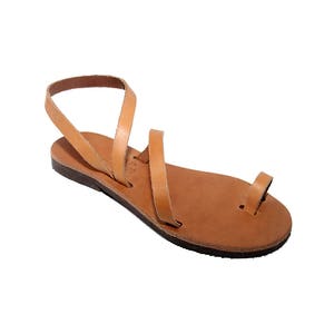 Puede incluir: Sandalias de cuero color canela con un dise&ntilde;o sencillo y una tira entre los dedos. Las sandalias tienen una suela plana y est&aacute;n hechas de una sola pieza de cuero.