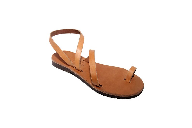 Puede incluir: Sandalias de cuero color canela con un dise&ntilde;o sencillo y una tira entre los dedos. Las sandalias tienen una suela plana y est&aacute;n hechas de una sola pieza de cuero.