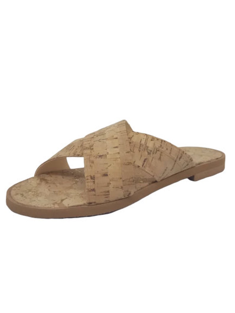 May include: Tan cork sandals with a criss-cross strap design. The sandals have a flat sole.