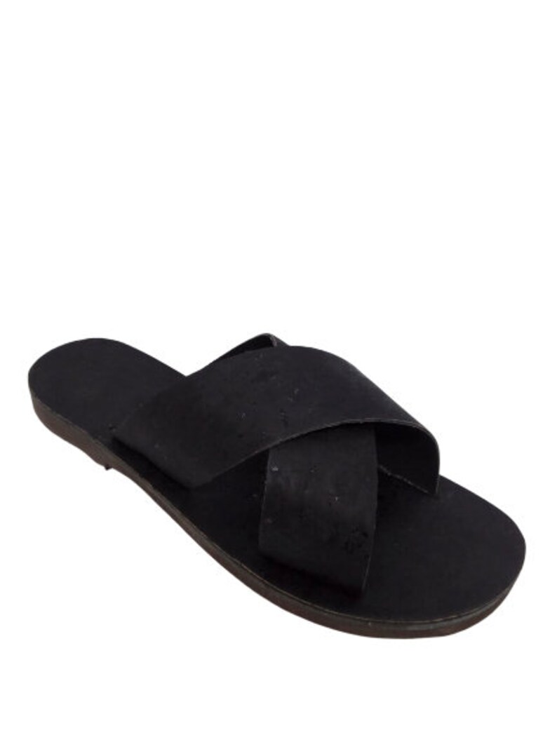 May include: Black leather sandals with a criss-cross strap design. The sandals have a flat sole and a cork-like texture.