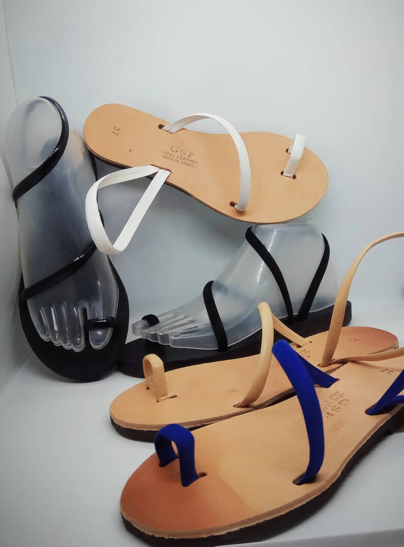 Puede incluir: Tres pares de sandalias de cuero con correas de diferentes colores. Las sandalias tienen un bucle para el dedo del pie y est&aacute;n hechas en Grecia. El texto en las sandalias dice "GSF Real Leather Made in Greece".