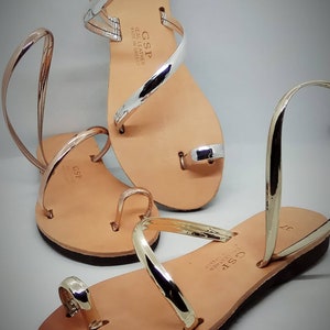 Puede incluir: Dos pares de sandalias de cuero con tiras doradas y plateadas. Las sandalias est&aacute;n hechas en Grecia y tienen el nombre de la marca "GSP" en las tiras.