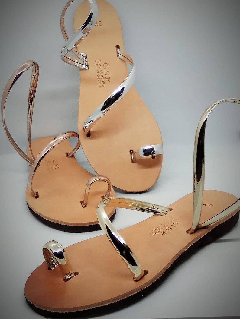 Puede incluir: Dos pares de sandalias de cuero con tiras doradas y plateadas. Las sandalias est&aacute;n hechas en Grecia y tienen el nombre de la marca "GSP" en las tiras.