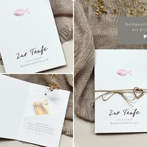 Könnte beinhalten: Weiße Karte mit einer rosa Fischillustration und dem Schriftzug "Zur Taufe". Die Karte ist mit Bindfaden und einem Holzherz gebunden. Die Karte ist für eine Taufe.