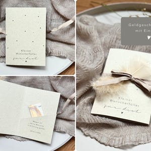 Könnte beinhalten: Eine beige Geschenkkarte mit schwarzen Punktakzenten und dem Text "Kleiner Wunscherfüller für dich" in handschriftlicher Schrift. Die Karte ist mit einem Band gebunden und mit Federn verziert. Die Karte ist für Geld konzipiert.