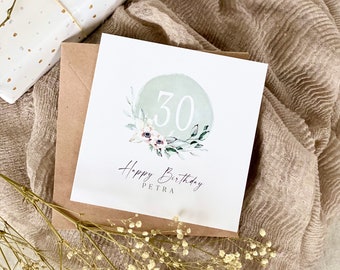 May include: A white card with a green watercolor circle with the number 30 in white. The circle is surrounded by green leaves and white flowers. The text "Happy Birthday Petra" is written below the circle.