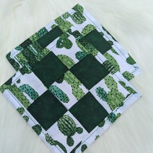 May include: Two green and white checkered fabric coasters with a cactus print. The coasters are made of a soft, cotton fabric and are perfect for protecting surfaces from heat and spills.