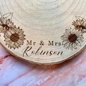 May include: A wooden round slice with a burnt-in design of sunflowers and the text "Mr & Mrs Robinson".