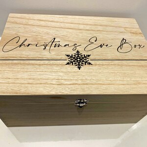 May include: A wooden box with a hinged lid and a metal clasp. The box is decorated with the text "Christmas Eve Box" and a snowflake design.