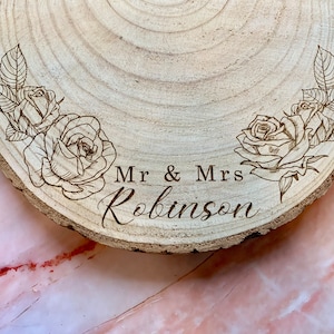 May include: A wooden slice with a natural bark edge, engraved with the text "Mr & Mrs Robinson" and two floral designs featuring roses.