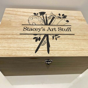 May include: A wooden box with a hinged lid and a metal latch. The box is decorated with a black and white design of art supplies, including paintbrushes, a paint palette, and a rolled-up canvas. The text "Stacey's Art Stuff" is printed on the box.