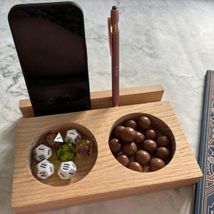 May include: A wooden organiser with two compartments, one for dice and one for small sweets. A black smartphone and a rose gold stylus are also included.