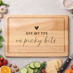Puede incluir: Tabla de cortar de madera con el texto "OFF MY TITS on picky bits" rodeada de ingredientes frescos como uvas, fresas, limones y tomates. También hay un cuchillo y galletas saladas.