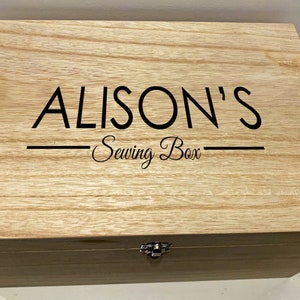 Peut inclure: Une bo&icirc;te en bois avec un couvercle &agrave; charni&egrave;res et un fermoir en m&eacute;tal. La bo&icirc;te est &eacute;tiquet&eacute;e "ALISON'S Sewing Box" en lettres noires.