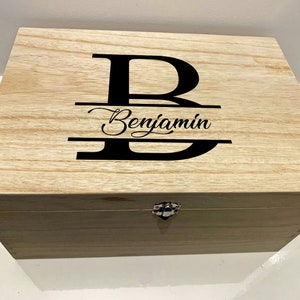 Puede incluir: Una caja de madera con tapa abatible y cierre de metal. La tapa está decorada con una letra "B" negra y el nombre "Benjamin" escrito en letra cursiva.