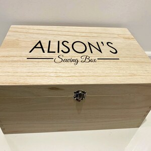 Peut inclure: Une bo&icirc;te en bois avec un couvercle &agrave; charni&egrave;res et un loquet en m&eacute;tal. La bo&icirc;te est de couleur brun clair et porte la mention "ALISON'S Sewing Box" grav&eacute;e sur le dessus.