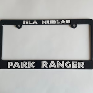 May include: Black plastic license plate frame with white text that reads "Isla Nublar" at the top and "Park Ranger" at the bottom.