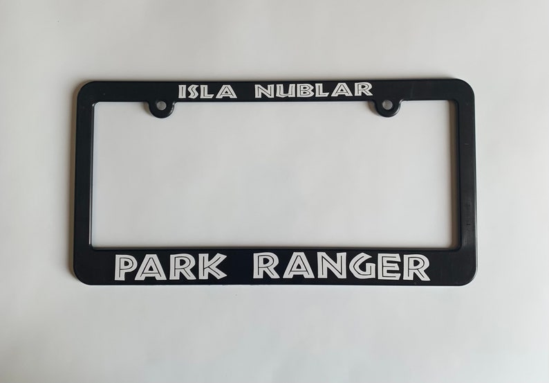 May include: Black plastic license plate frame with white text that reads "Isla Nublar" at the top and "Park Ranger" at the bottom.