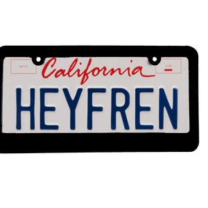May include: A black license plate frame with a white background. The plate says "California" in red cursive and "HEYFREN" in blue block letters.