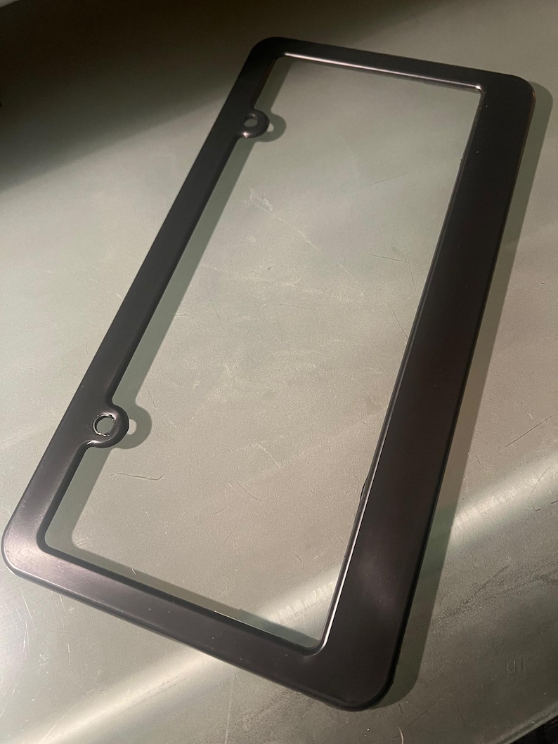 May include: Black plastic license plate frame with rounded corners and two holes on the top and bottom.