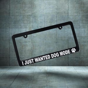 Może przedstawiać: Czarna ramka tablicy rejestracyjnej z białym napisem "I JUST WANTED DOG MODE". Biały odcisk łapy znajduje się po prawej stronie ramki. Ramka jest prostokątna z zaokrąglonymi rogami.